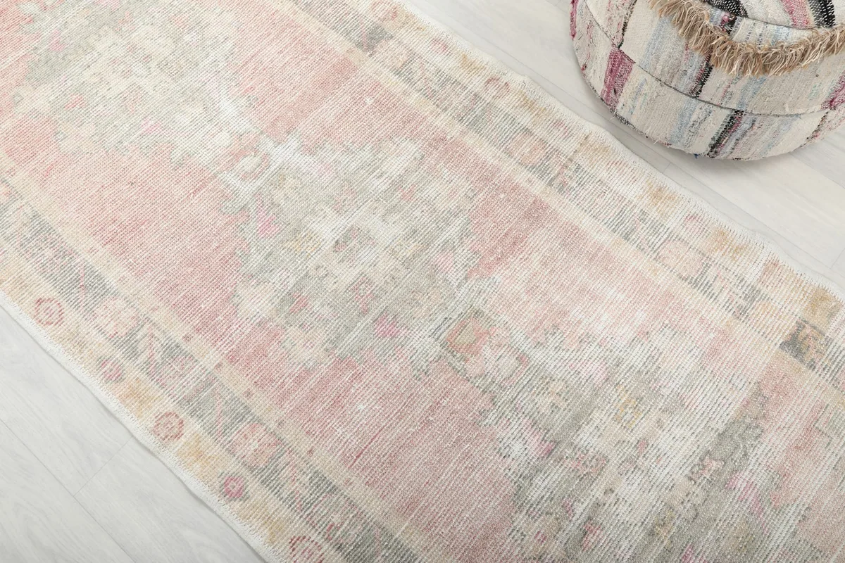 Close-up of the vintage rug's faded pink, gray, and beige geometric patterns and texture.