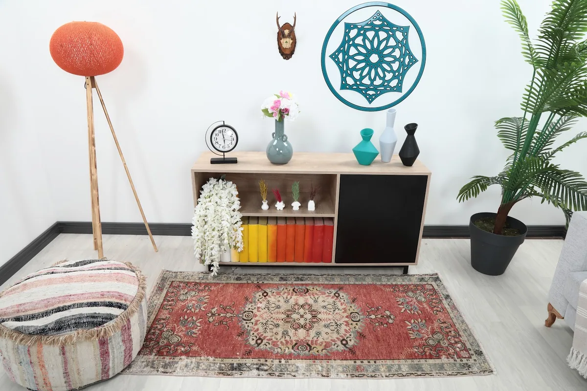 Rust area rug placed in a modern living room setting with a light wood cabinet and pouf