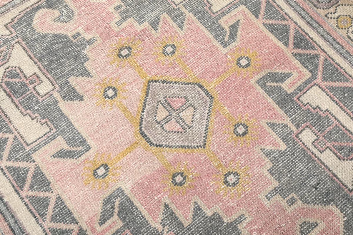 Detailed view of the central pink and charcoal geometric medallion with yellow accents