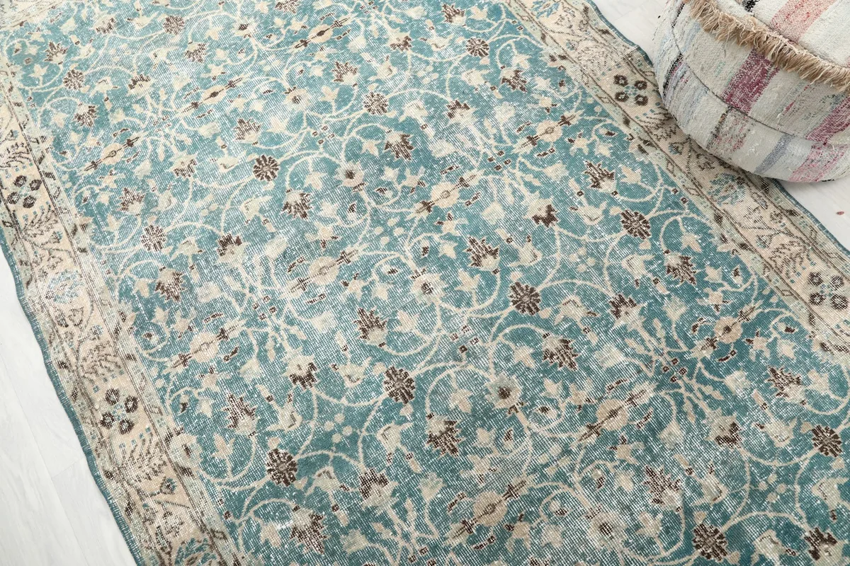 Angled view highlighting the blue field and beige border motifs of the vintage rug