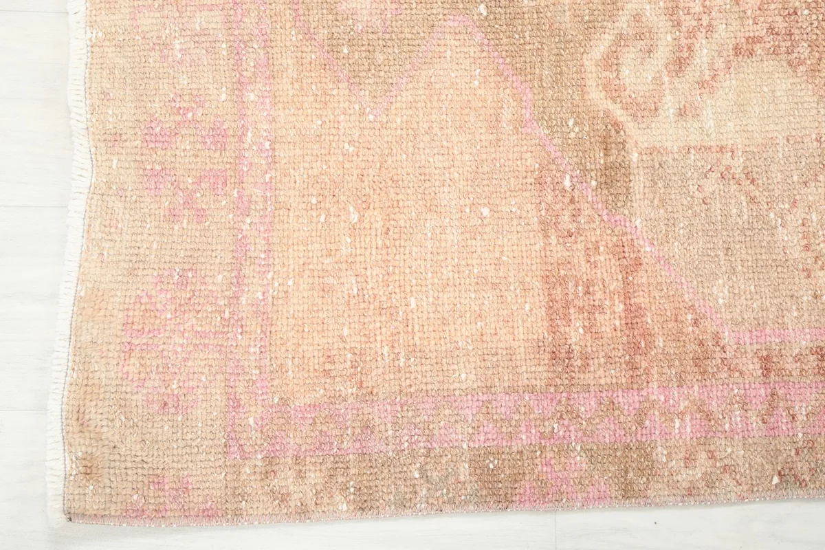 Detail of the rug's edge and border, displaying the muted rose and beige hues.