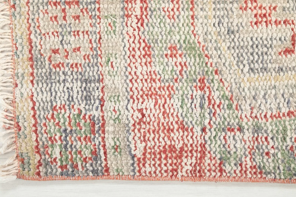 Close-up of the low pile and texture, showing the individual knots and the blend of orange, beige, and green threads.