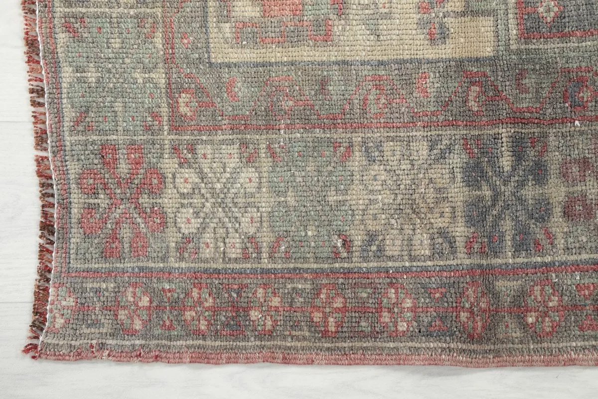 Detail of the rug's border, featuring geometric motifs in red, gray, and beige tones.
