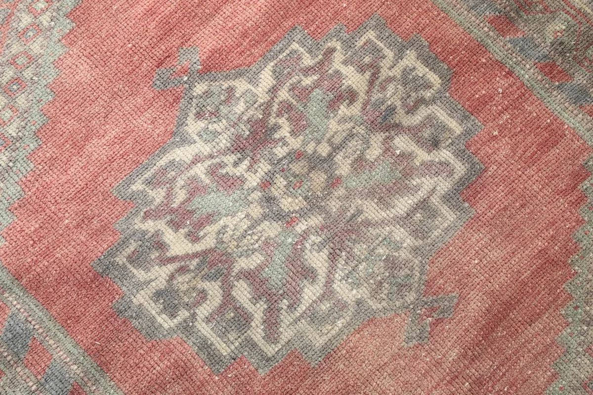 Close-up of the rug's low wool pile, showing the texture and faded colors of the medallion.
