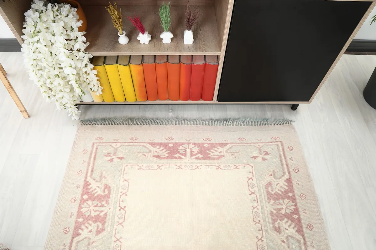 View of the rug's end with fringe, positioned in front of a cabinet with colorful books