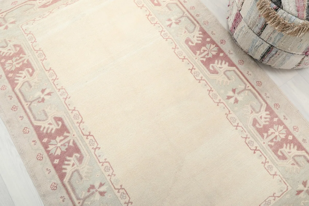 Detailed angle view of the rug's ivory field and rose geometric border patterns