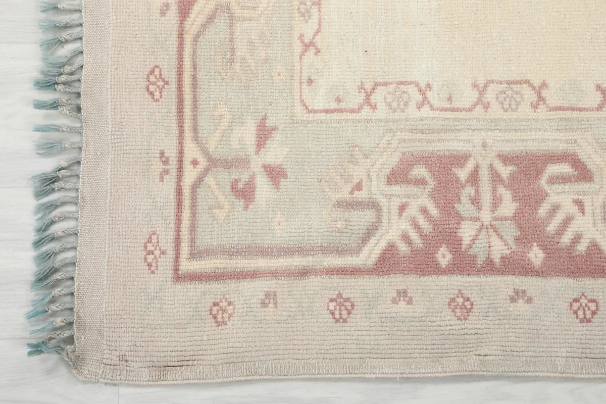 Detailed view of the rug's corner, showcasing the rose and beige geometric motifs in the border