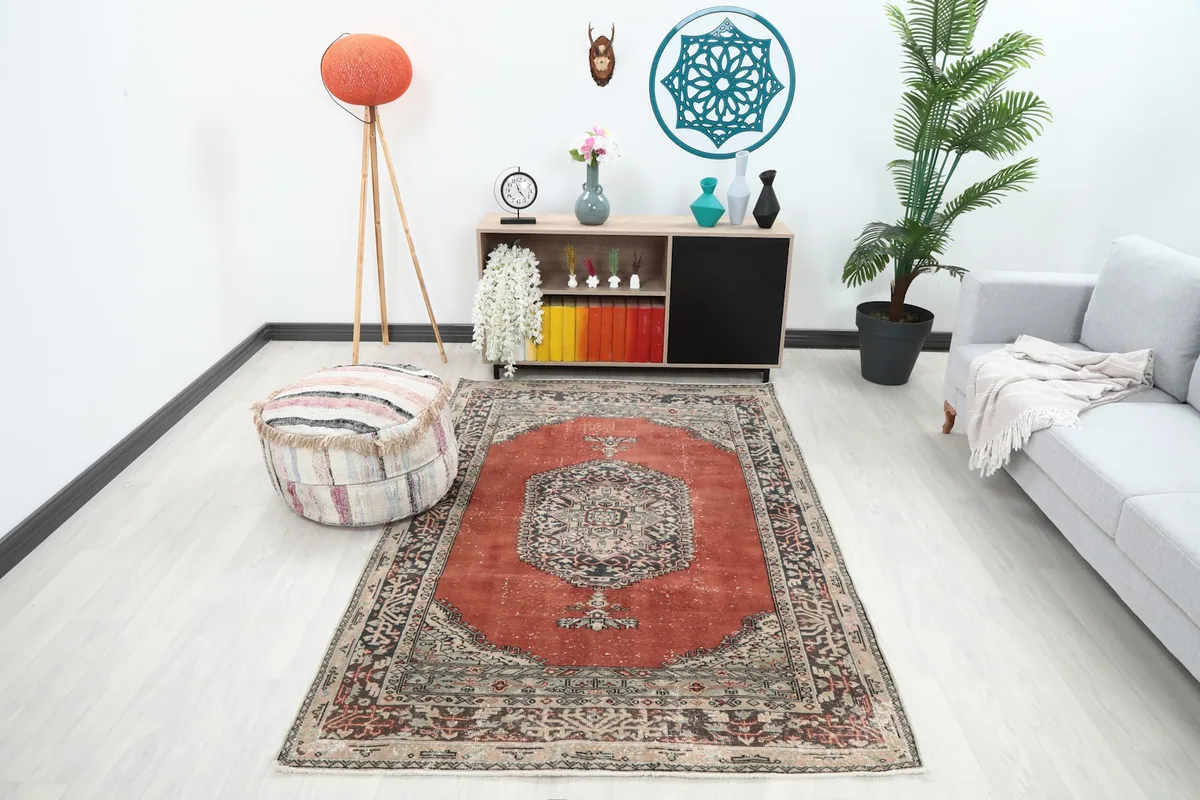 Vintage rust area rug displayed in a living room setting with a light sofa and pouf.