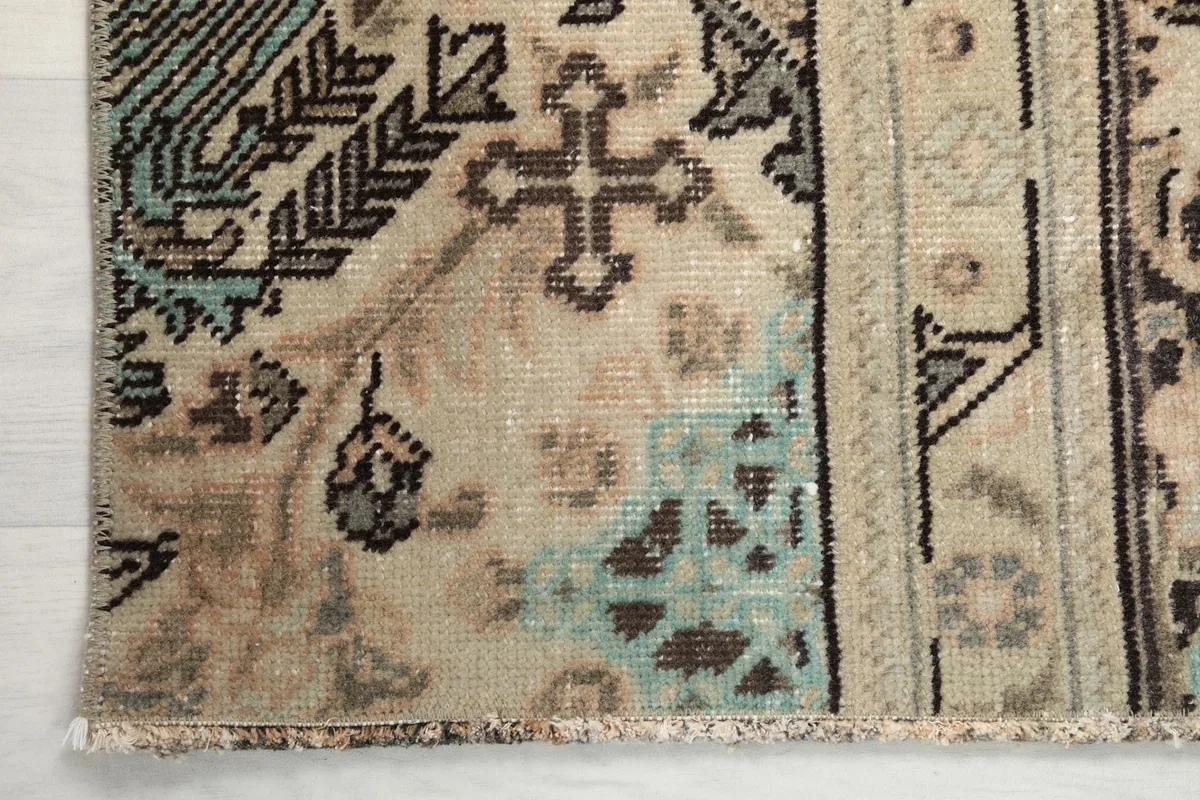 Detail shot of the rug's corner with fringe, showing color variations and wear