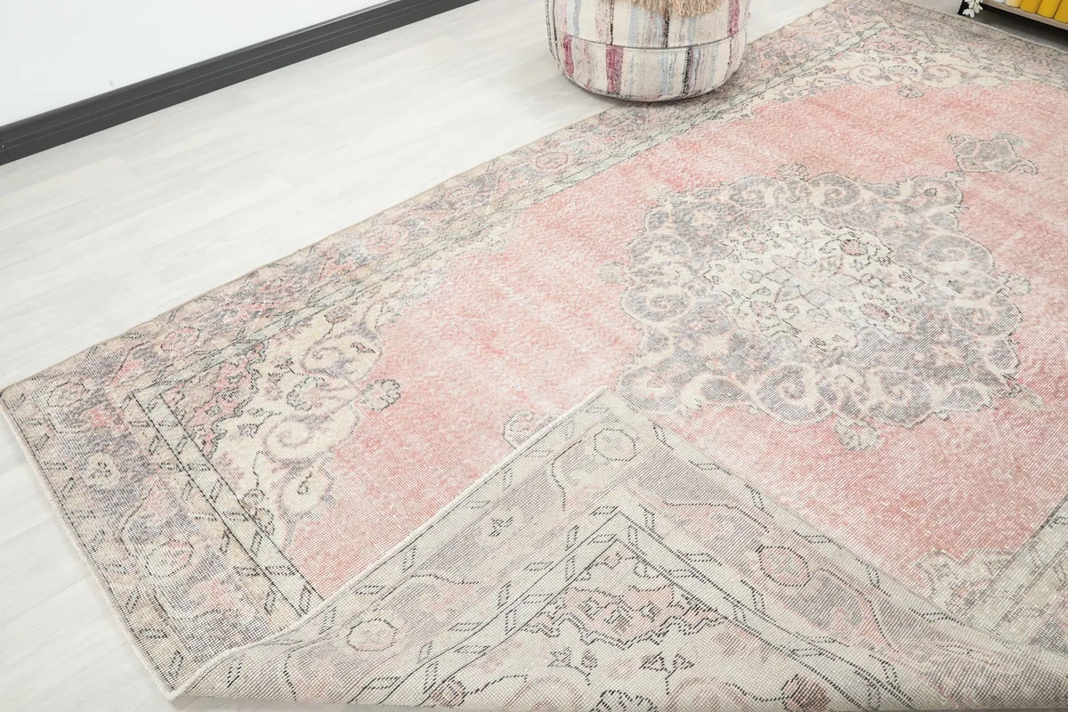 Corner of the rose and gray vintage rug folded back, revealing the cotton foundation and hand-knotted construction.