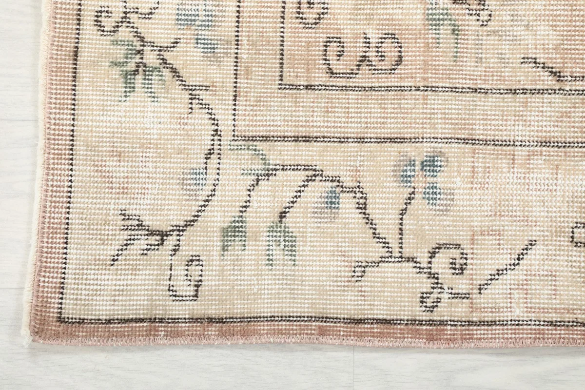 Close-up of a corner of the rug, showing the beige border with vine patterns and the finished edge.