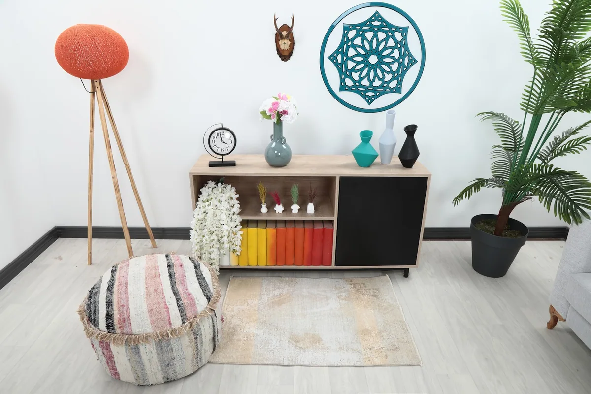 Vintage beige and tan rug placed in a living room setting under a media console with a striped pouf.