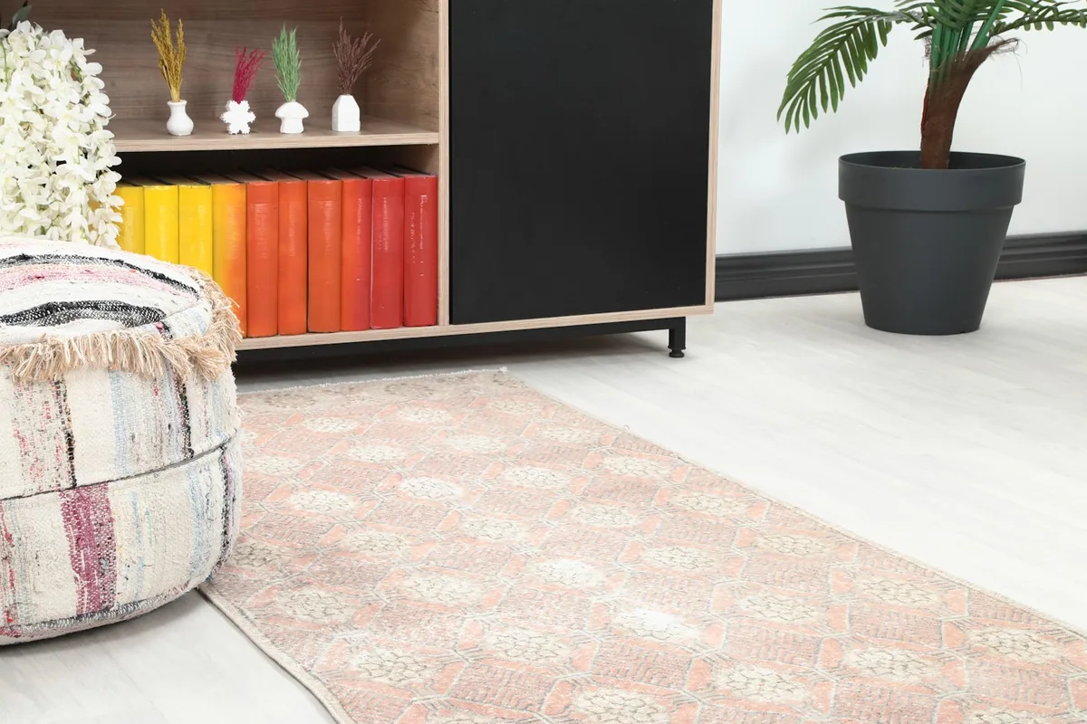 Close-up of the runner rug's end near a decorative pouf and wooden cabinet in a room.