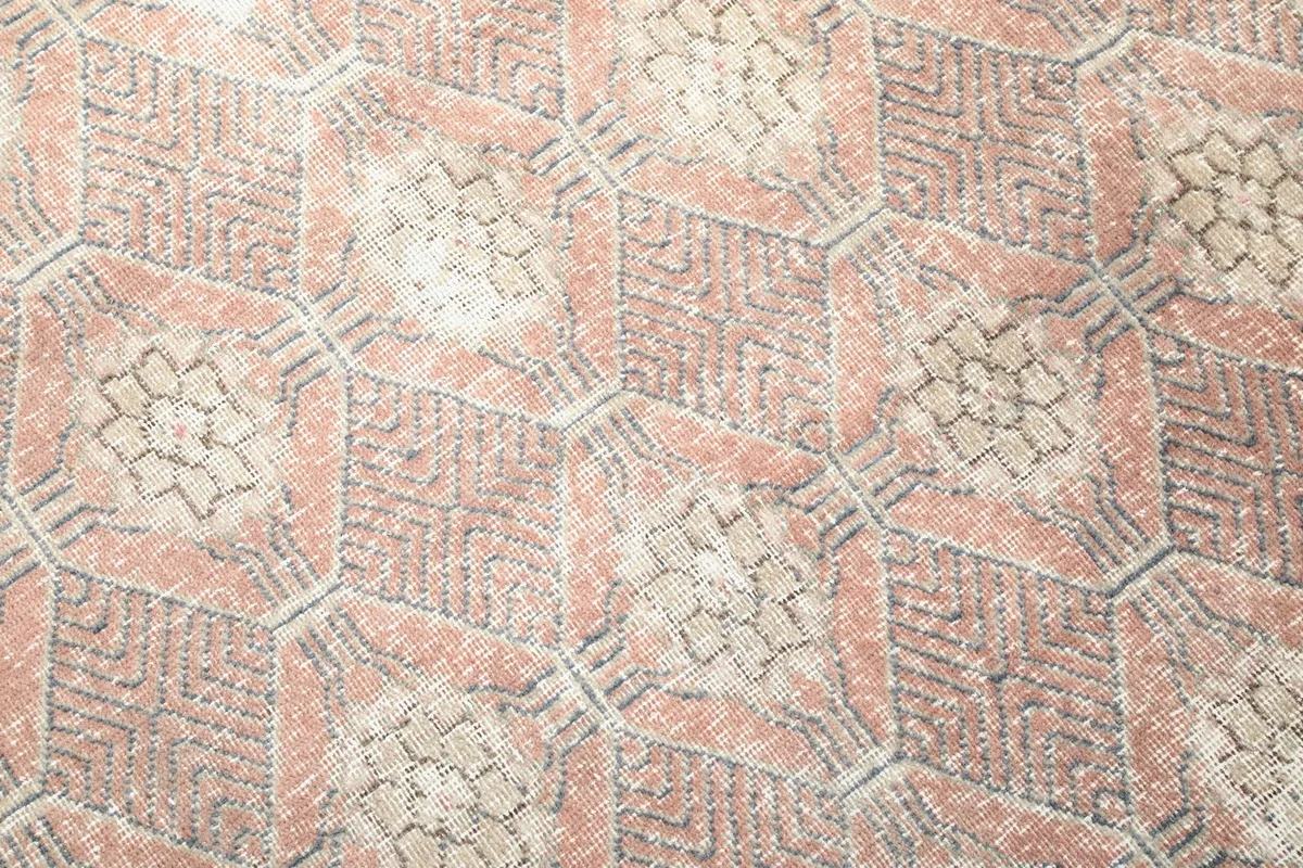 Close-up detail of the hand-knotted geometric pattern in rose, beige, and cream colors.