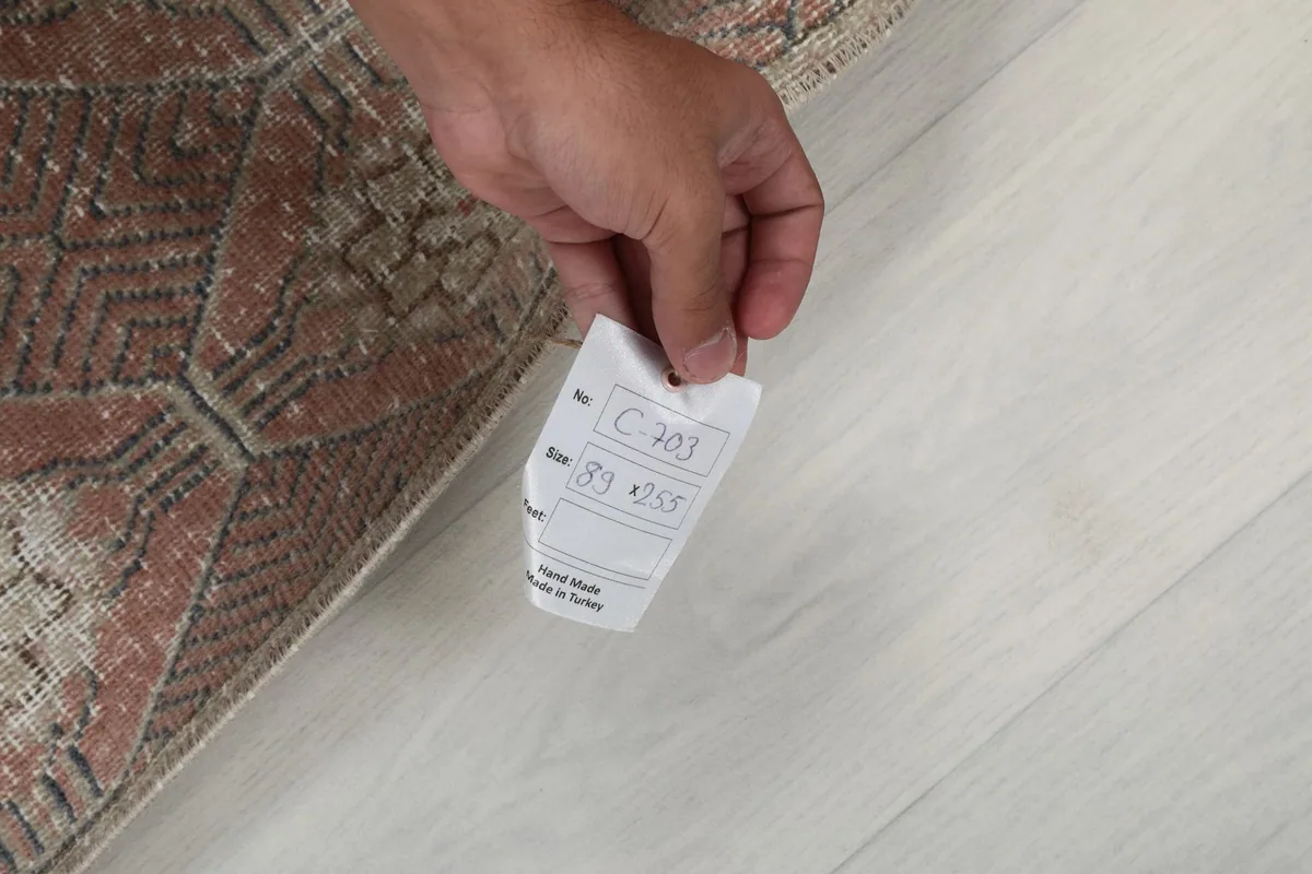 Hand holding a tag with the rug's dimensions and origin, showing the quality of the piece.