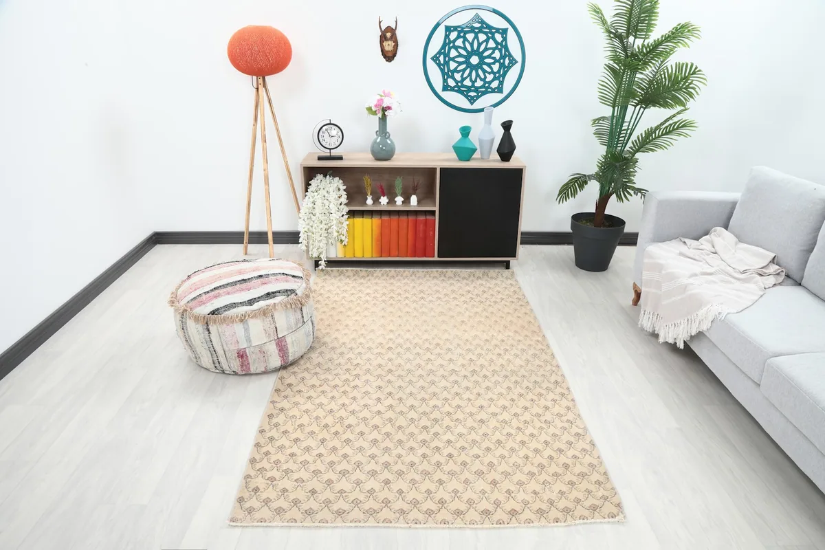 Vintage beige and rose area rug displayed in a modern living room setting with a sofa and pouf.
