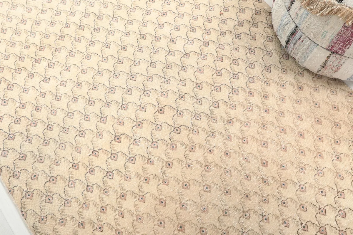 Detailed view of the repeating rose and green/blue motifs on the beige field of the vintage rug.