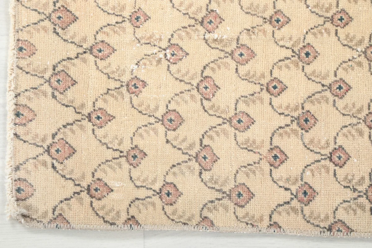 Corner detail of the vintage beige rug, highlighting the edge finishing and pattern clarity.