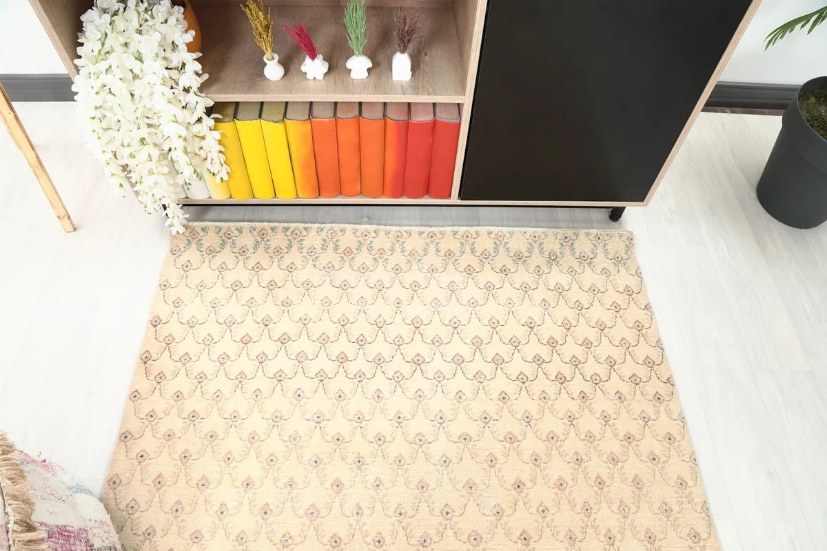 Overhead view of the beige vintage rug showing its repeating rose and green/blue pattern in a room setting.