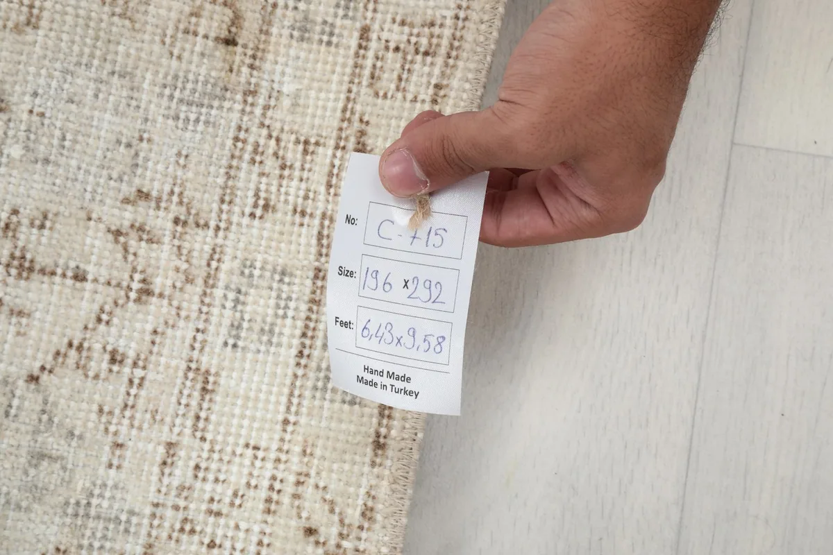 Hand holding a tag with the rug's dimensions and origin, confirming it is hand-made in Turkey.