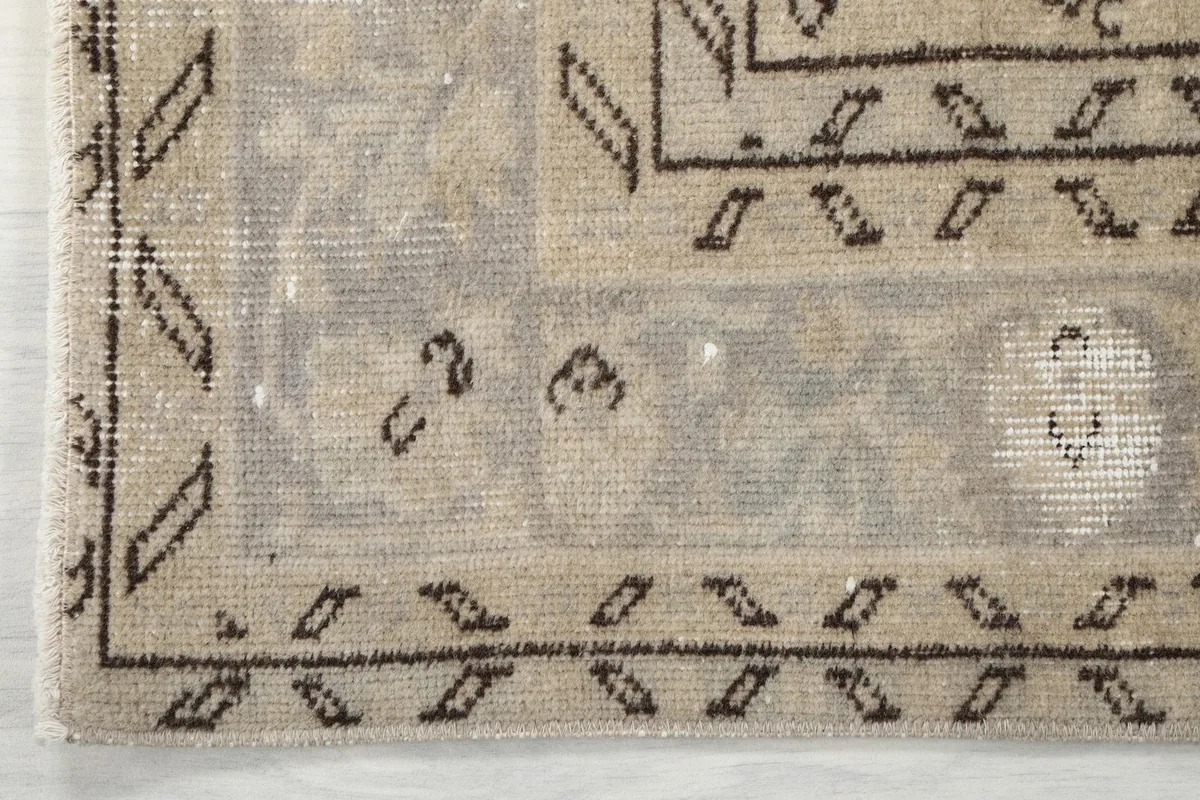 Corner detail of the rug's border, featuring geometric patterns in gray and ivory.
