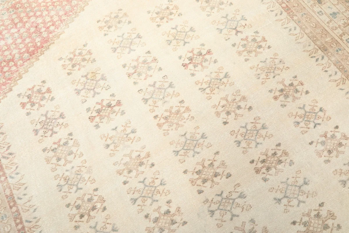 Detailed view of the ivory field with repeating geometric motifs in rose, tan, and blue