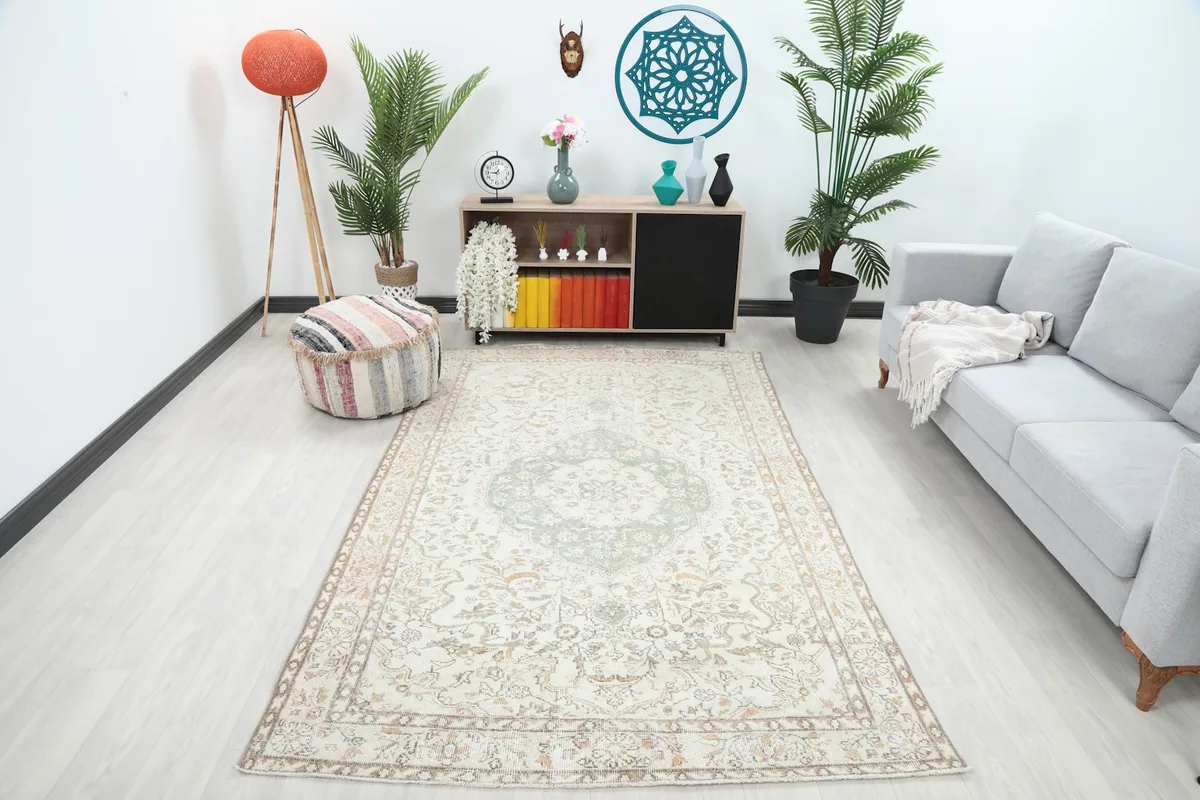 Vintage ivory and green rug displayed in a room setting with a sofa and plants