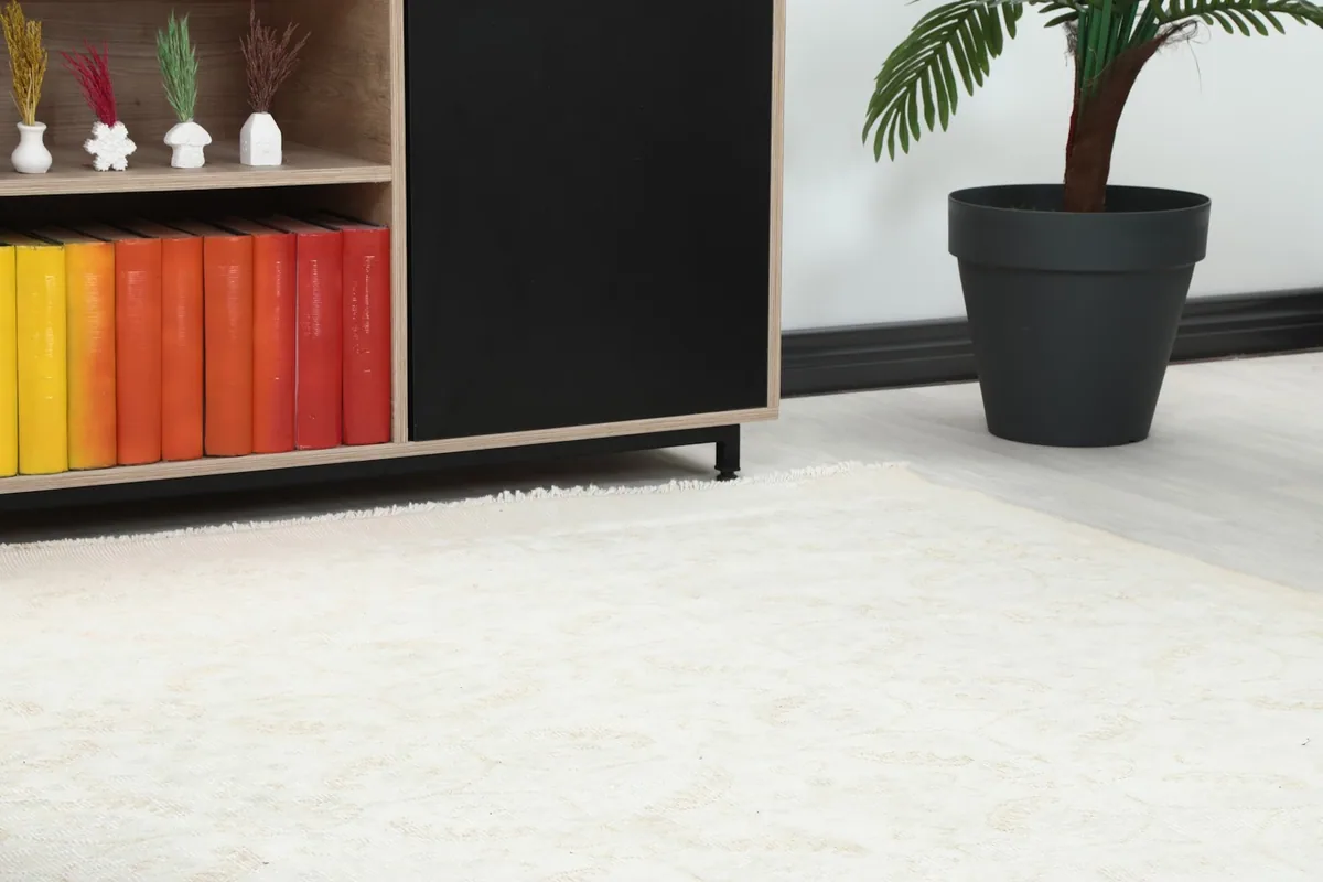 Close-up of the rug's subtle beige and ivory patterns near a wooden cabinet with colorful books.
