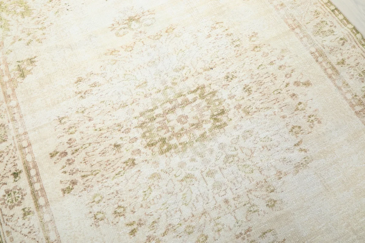 Close-up of the rug's central medallion-like pattern in ivory and olive tones, showing texture.
