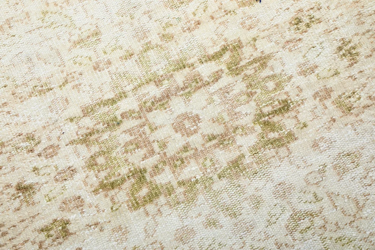 Detailed view of the faded olive and tan patterns within the rug's field, showcasing vintage wear.