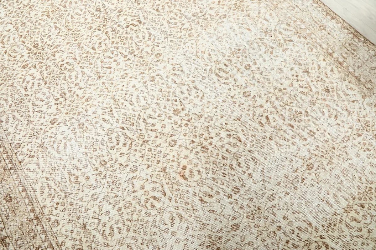 Detailed angled view of the ivory field and tan floral patterns of the vintage rug.