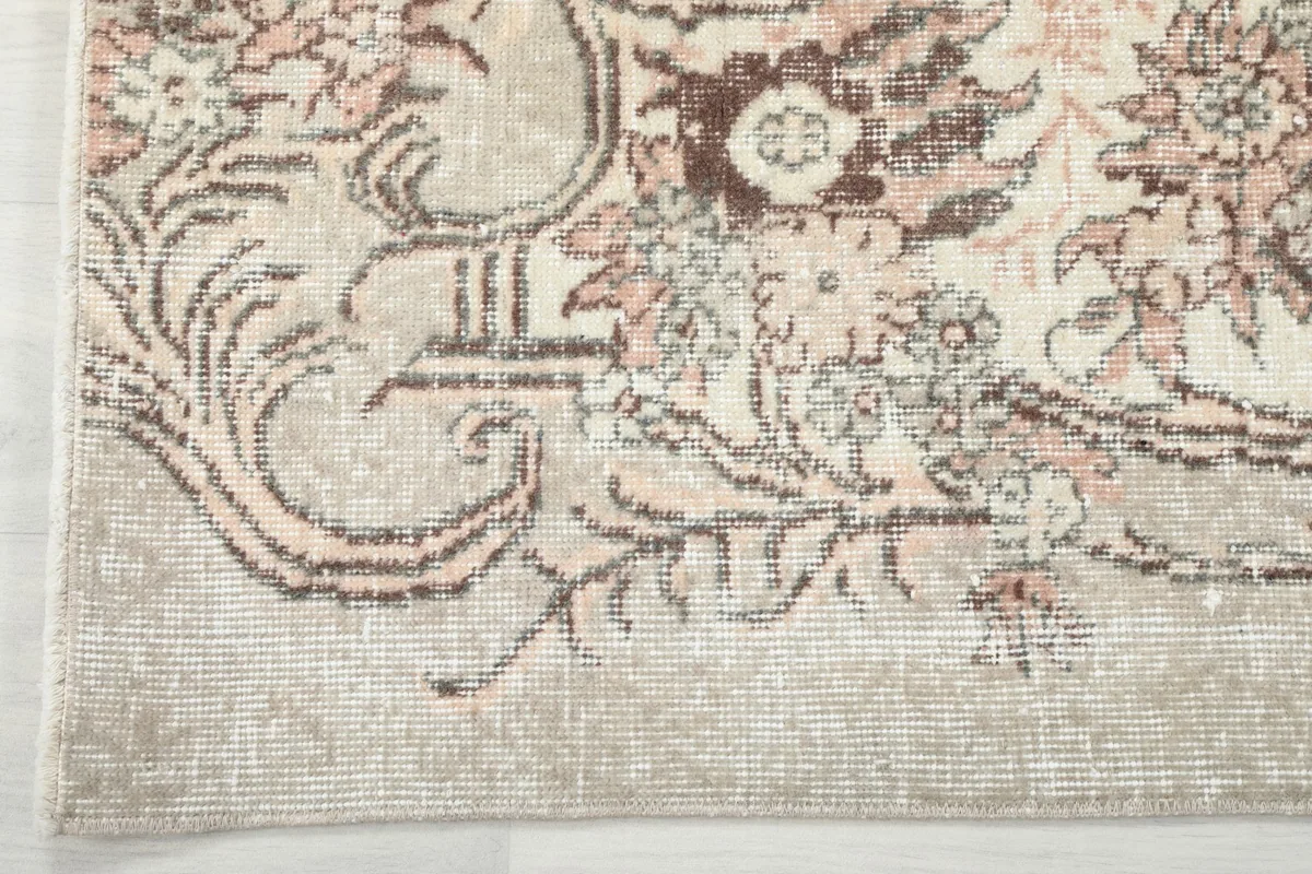 Detail of the rug's border design, featuring rose and brown floral motifs against a beige background