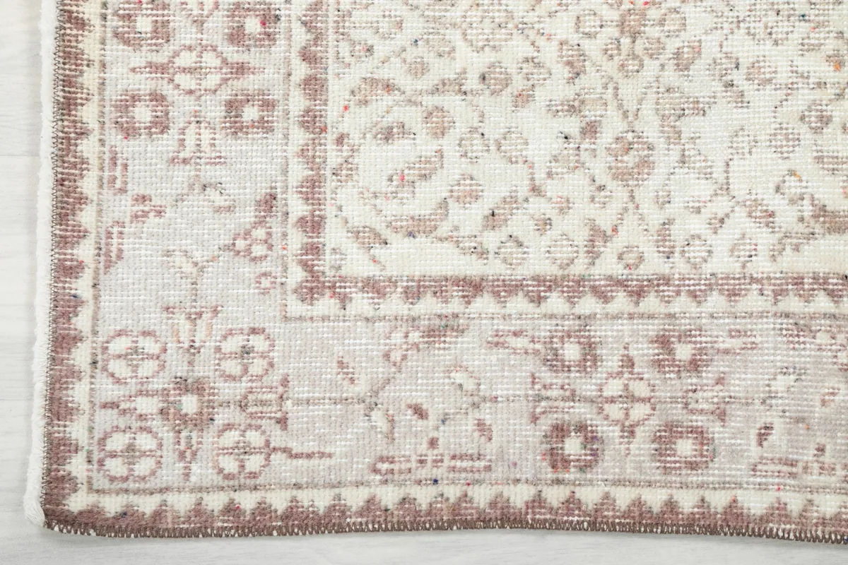 Detail of the rug's border, showcasing the geometric and floral elements in rose tones
