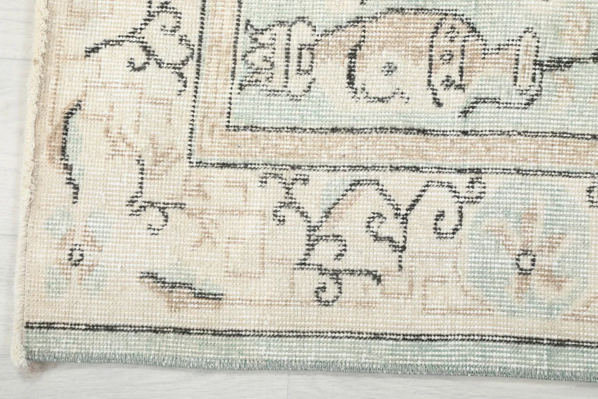 Corner detail of the rug, showing the beige border with charcoal patterns and the light blue field.