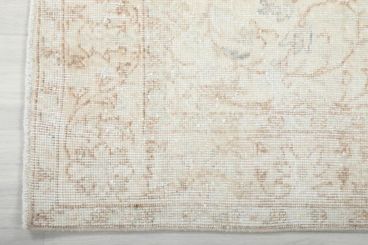Detail of the rug's border, featuring a delicate geometric pattern in muted beige and ivory