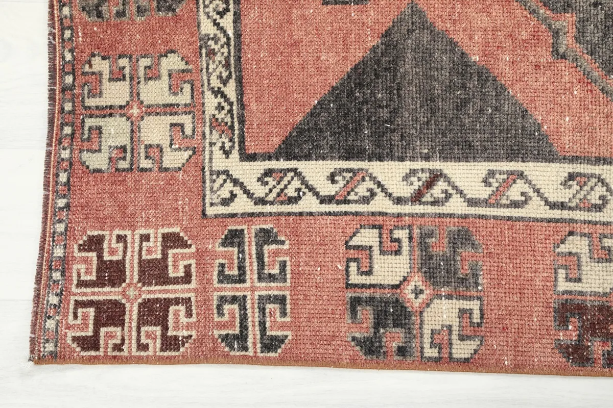Detailed view of the rug's border pattern in beige, black, and rust, showing the aged wool pile.
