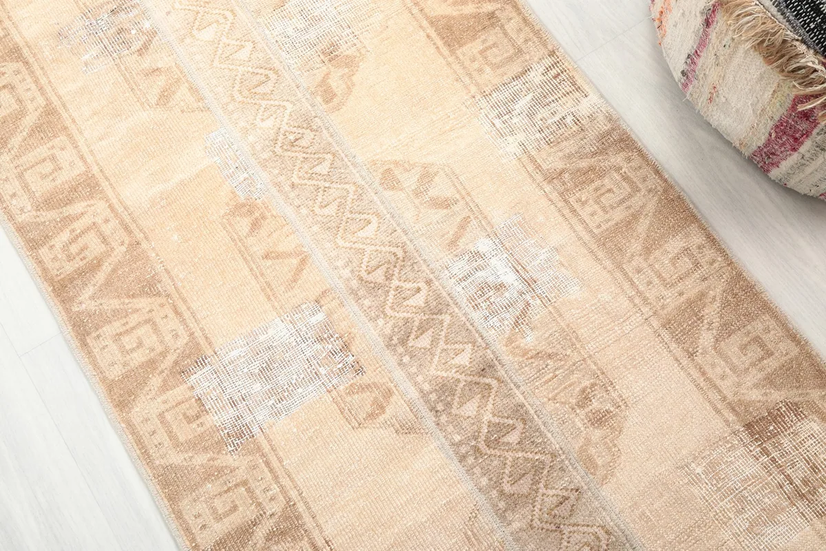 Detailed view of the geometric patterns and distressed areas on the beige runner rug