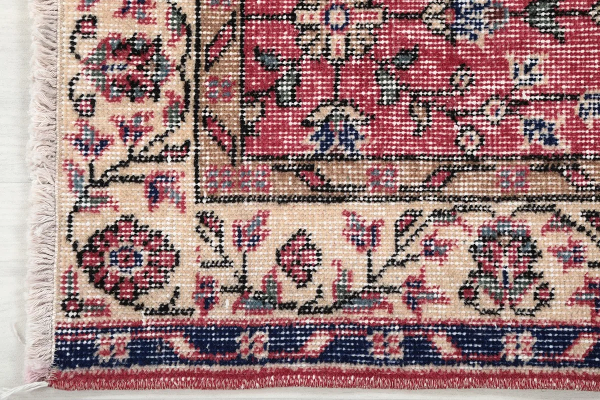 Close-up of the rug's border, featuring cream, navy, and rose floral designs.