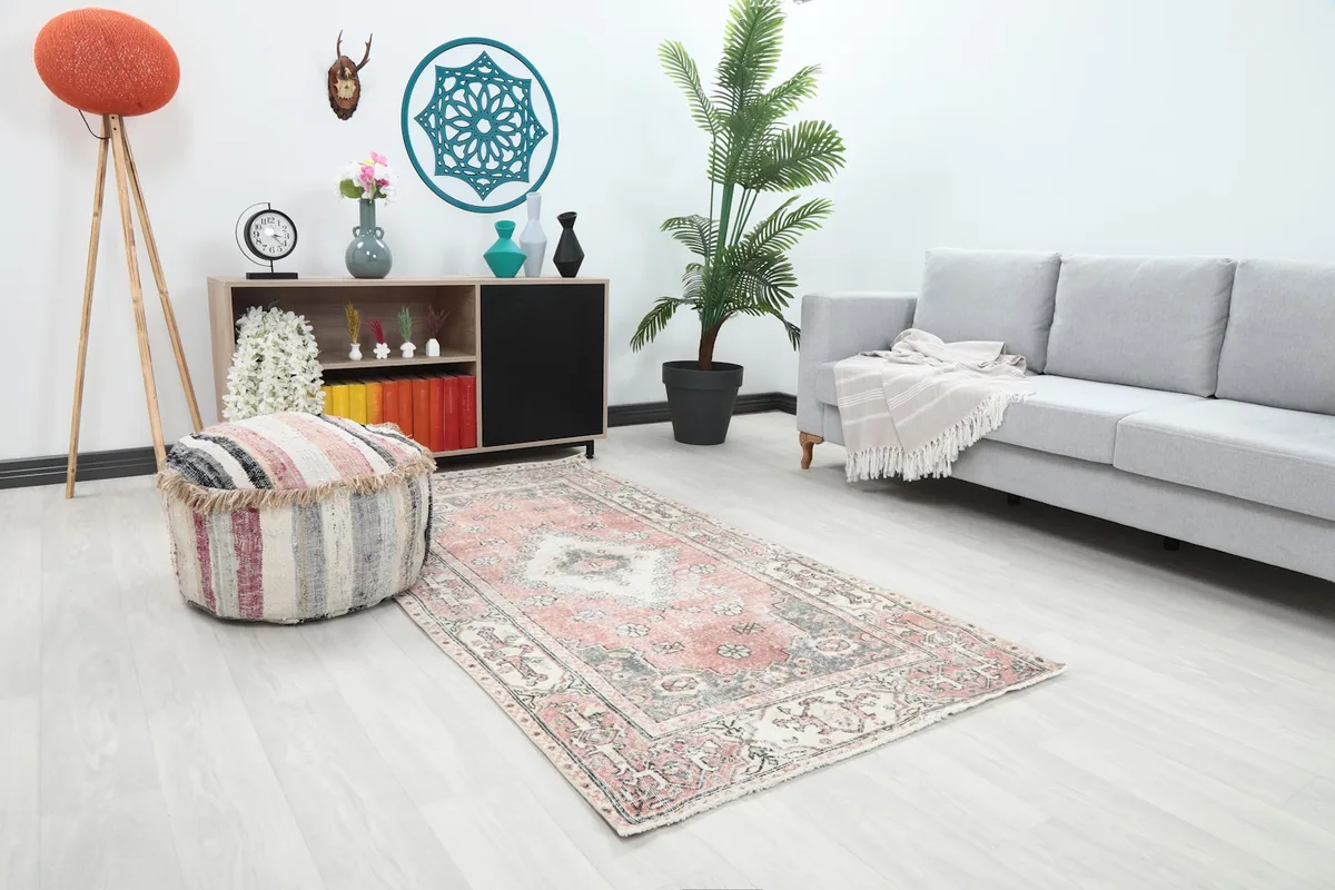 Angle view of the rose and gray vintage rug in a living space with a striped pouf