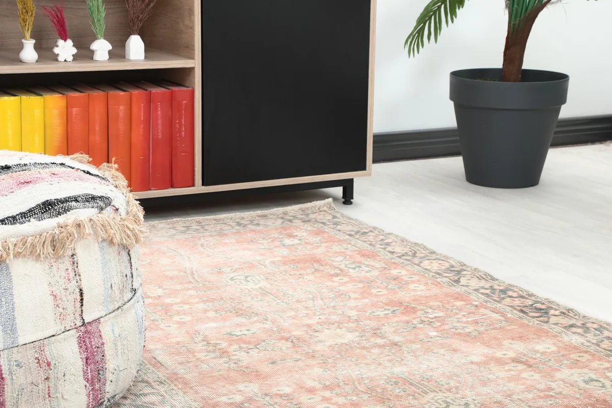 Close-up angle shot of the rose rug's pattern and border next to a decorative pouf