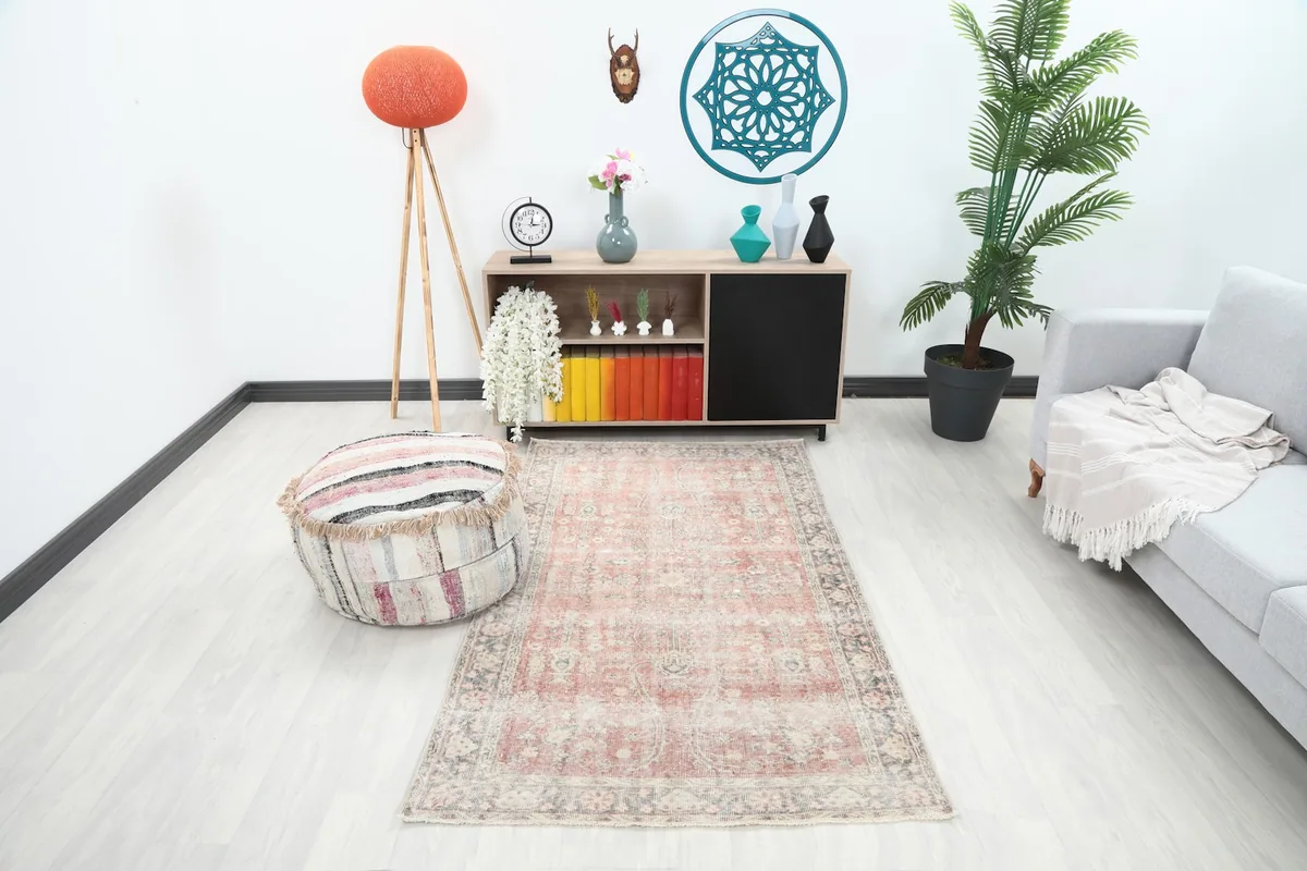 Vintage rose Anatolian rug displayed in a modern living room setting with a light sofa and pouf
