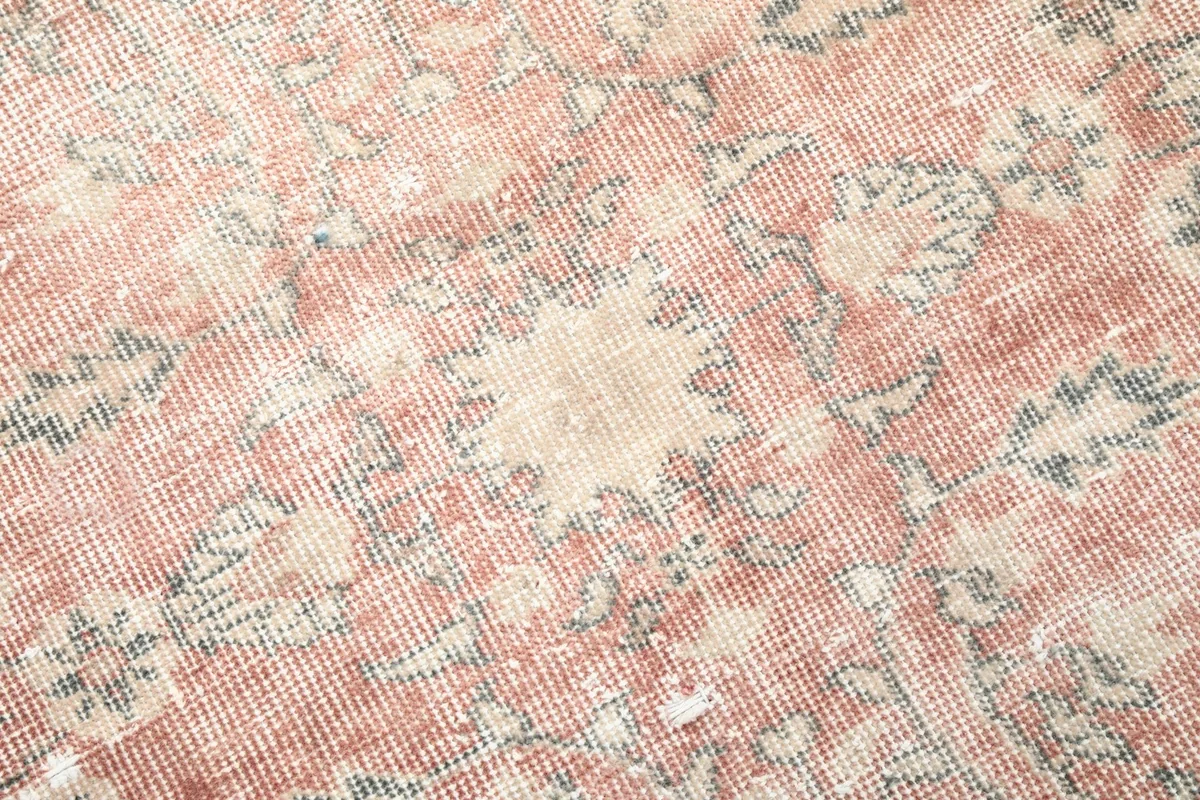 Close-up of the rug's central floral and geometric motifs in rose, beige, and gray tones