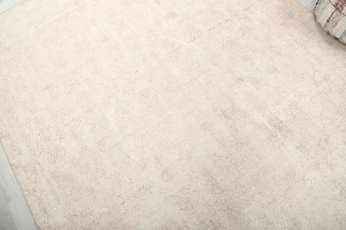 Close-up of the rug's surface, highlighting the faded ivory and rose geometric pattern and low pile.