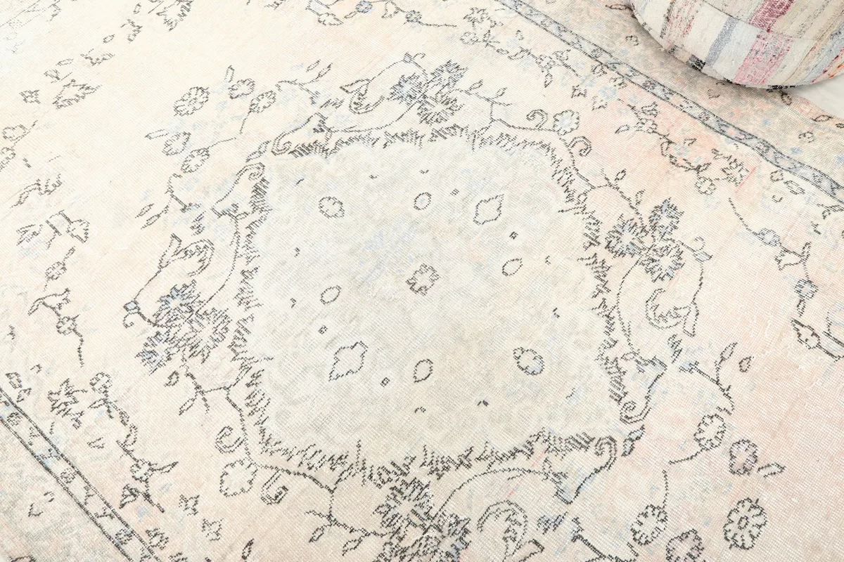 Detailed view of the central medallion design on the ivory rug, highlighting the faded colors.
