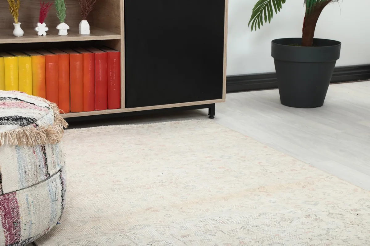Close-up of the ivory rug's subtle floral pattern and faded texture next to a pouf and cabinet.