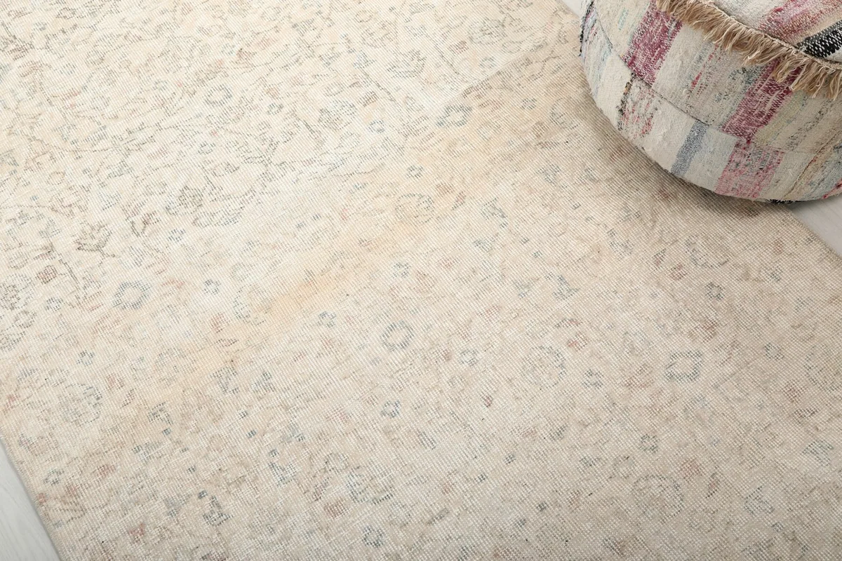Detailed view of the rug's surface, showing the faded ivory and beige tones with soft floral motifs.