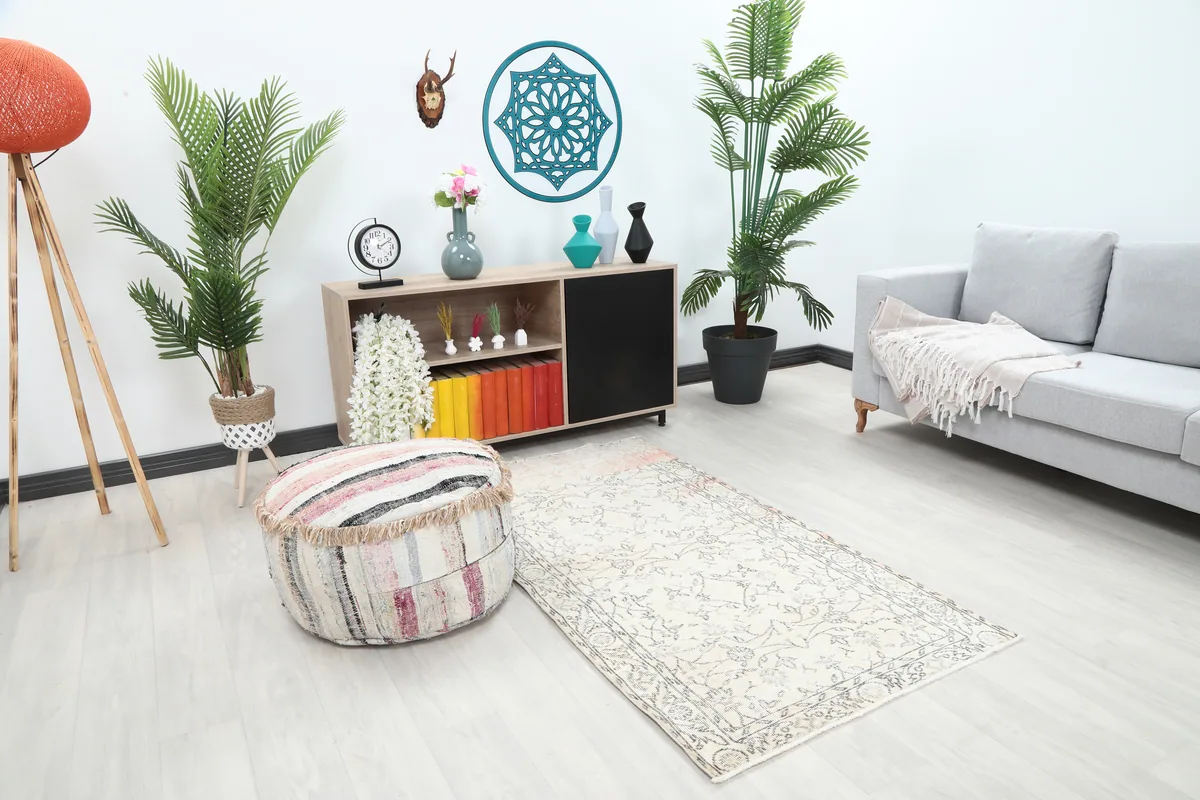 Faded Ivory Floral Anatolian Rug from a wider angle in a room setting with a pouf and sofa