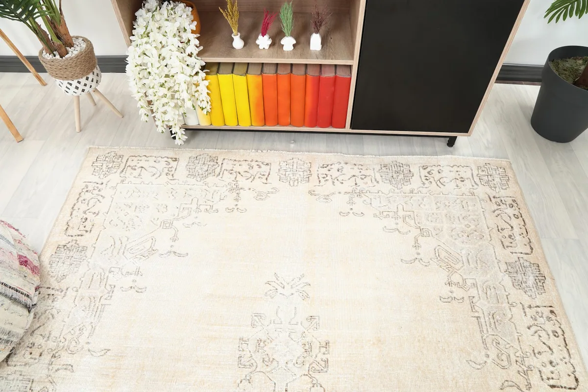 Upper section of the rug showing the border and faded motifs, next to a striped pouf.