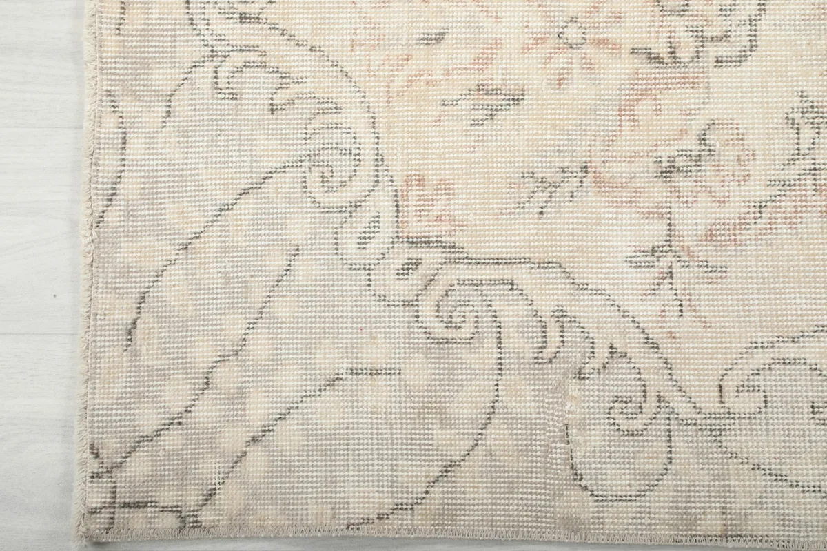 Detail of the rug's border with its faded, scroll-like patterns and visible hand-knotting.