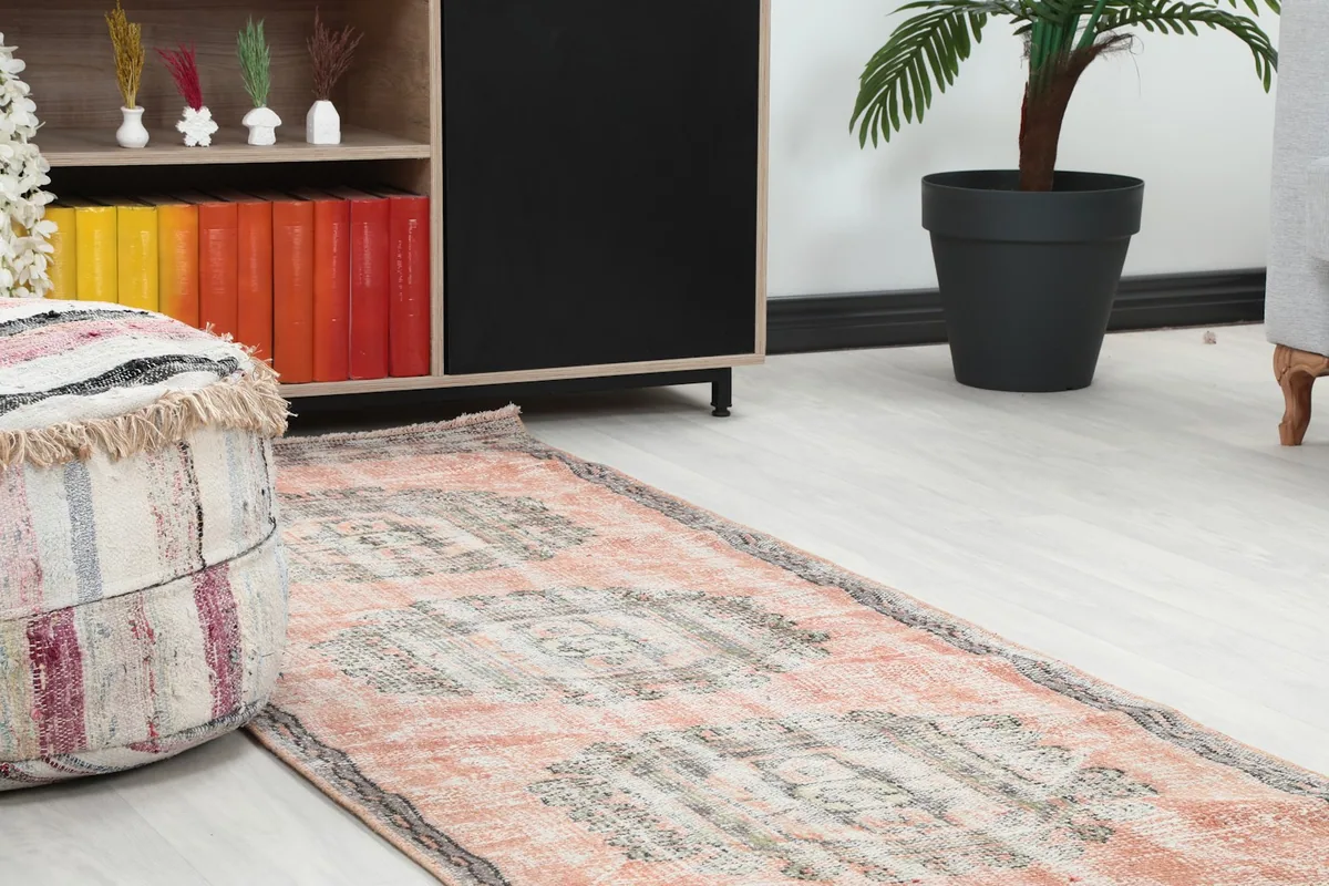 Close-up angle shot of the rose runner rug showing its texture and placement next to a decorative pouf and cabinet.